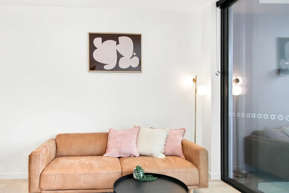 Bright living room with caramel sofa, soft pink cushions and abstract artwork